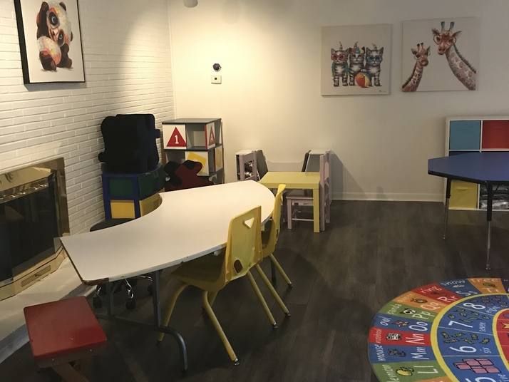 A playroom with dark plank floors, a white curved table with yellow chairs, a colourful alphabet rug and cat and giraffe pictures on the wall.